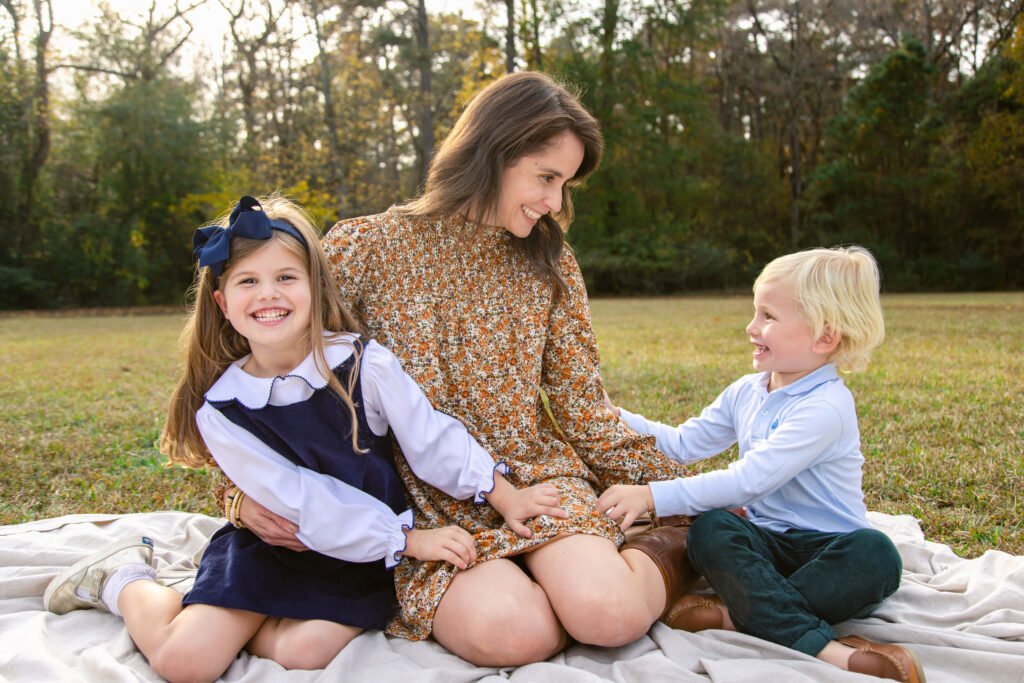 Woman laughing with her two children on a picnic blanket. The kids are all dressed in fall colors & corduroy and the mother is in an orange micro floral long sleeved dress. 